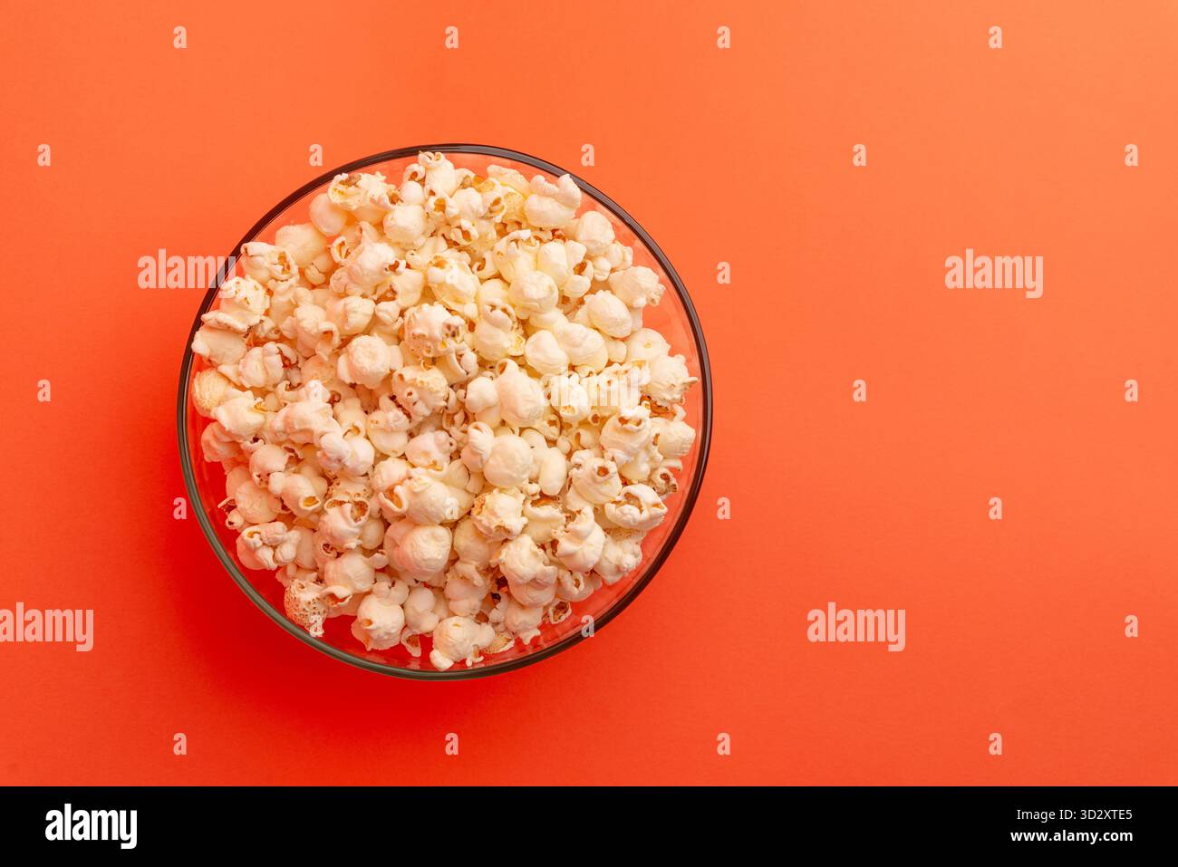 Vista dall'alto della ciotola di popcorn su sfondo arancione, composizione minimalista ideale per pubblicità di spuntini, immagini notturne di film o fotografie creative di cibo Foto Stock