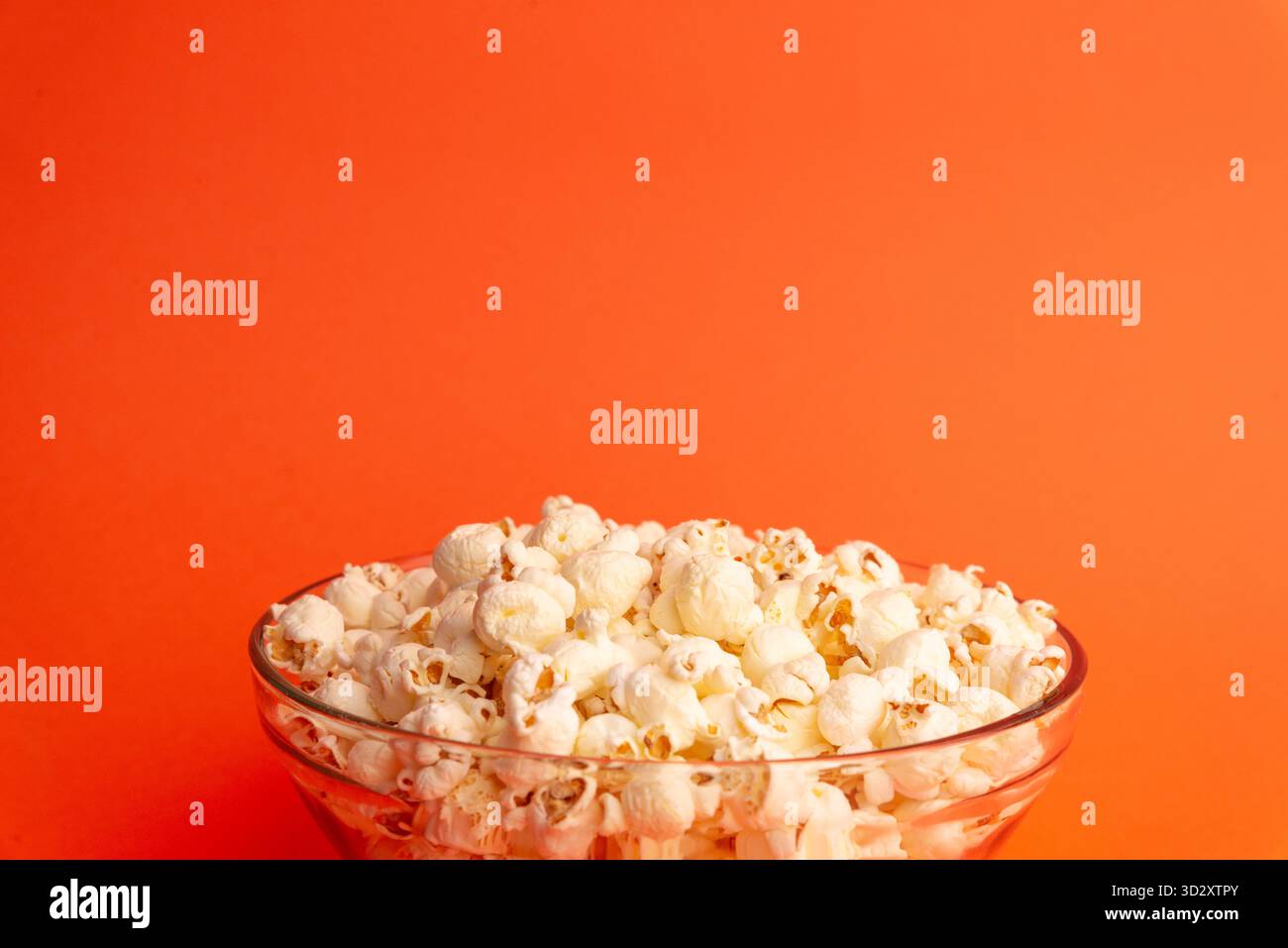 Primo piano di popcorn in una ciotola di vetro su sfondo arancione, che mostra consistenza, dettaglio e concetto alimentare, ideale per l'uso commerciale e creativo Foto Stock