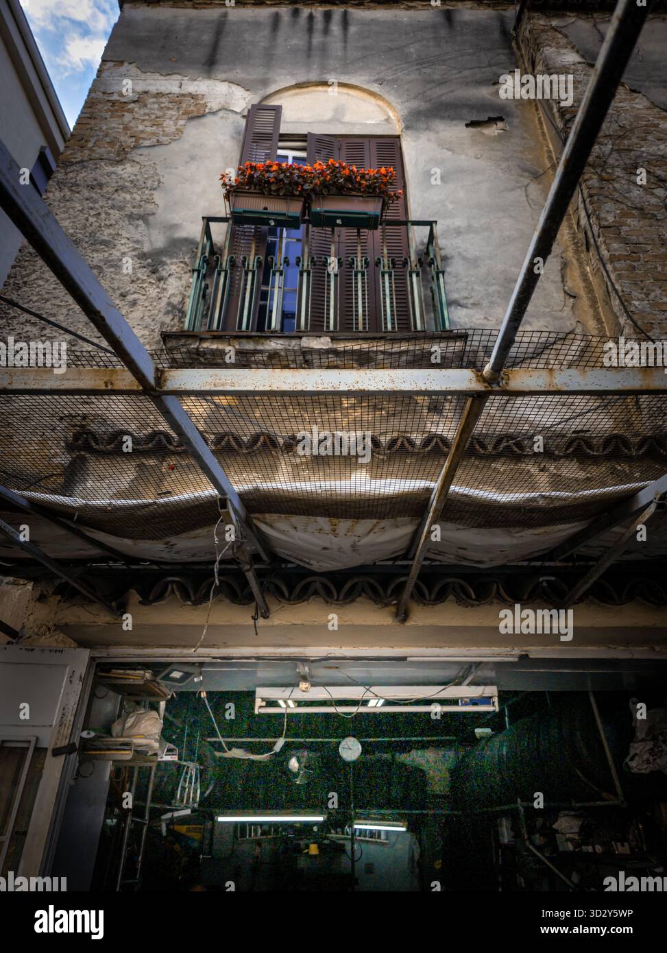 Un vecchio edificio in una strada di Belgrado con pareti incrinate e un piccolo balcone con persiane di legno chiuse e fiori rossi, vista dal basso Foto Stock