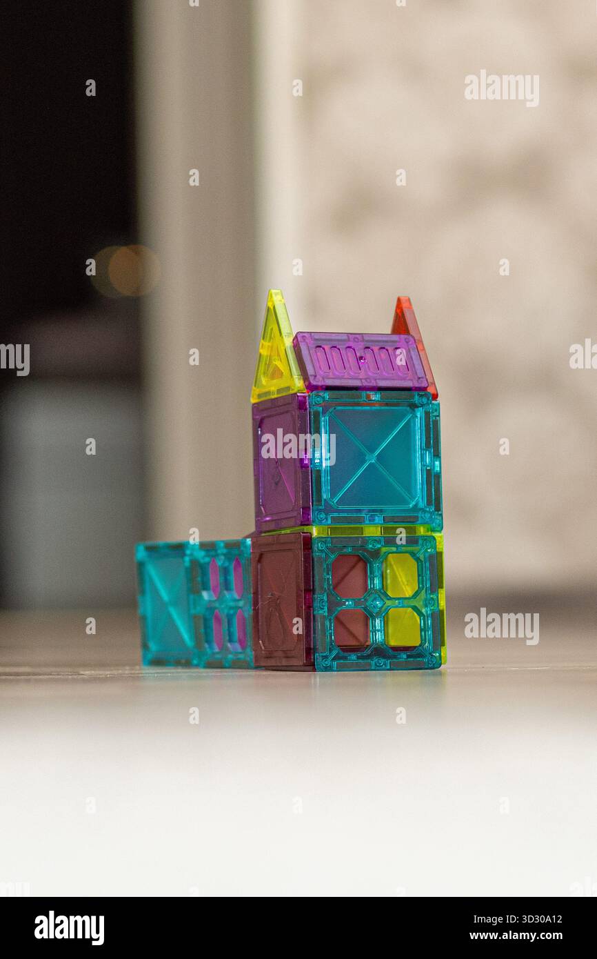 Blocchi magnetici dai colori vivaci sono disposti in modo creativo per formare una piccola struttura su un pavimento di legno liscio in una sala ben illuminata. Foto Stock