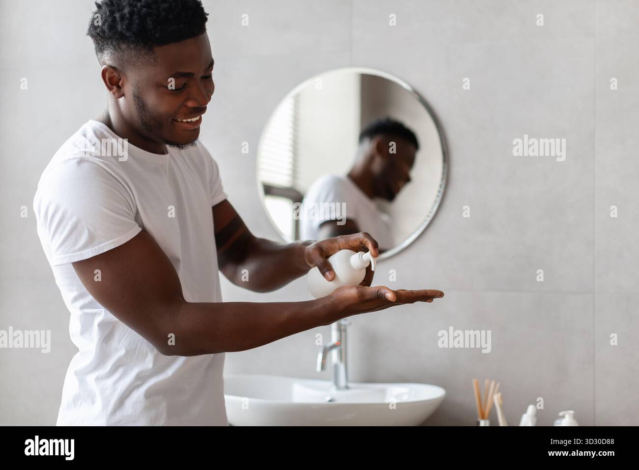Uomo africano che applica sapone liquido mentre si lava le mani in bagno a casa durante il giorno Foto Stock