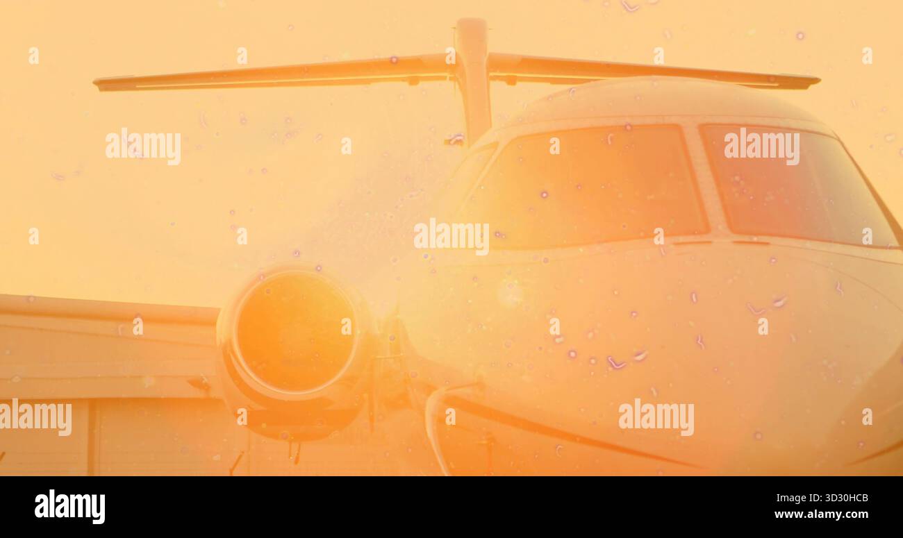 Seduto a un jet privato che riceve il bagliore del tramonto sull'asfalto con aspirazione motore, finestre della cabina di pilotaggio e hangar Foto Stock