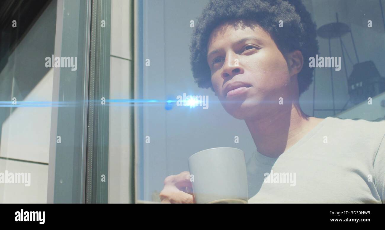 Uomo adulto in piedi che guarda fuori dalla finestra di vetro vicino alla lampada a sospensione negli interni di casa, tenendo la tazza Foto Stock