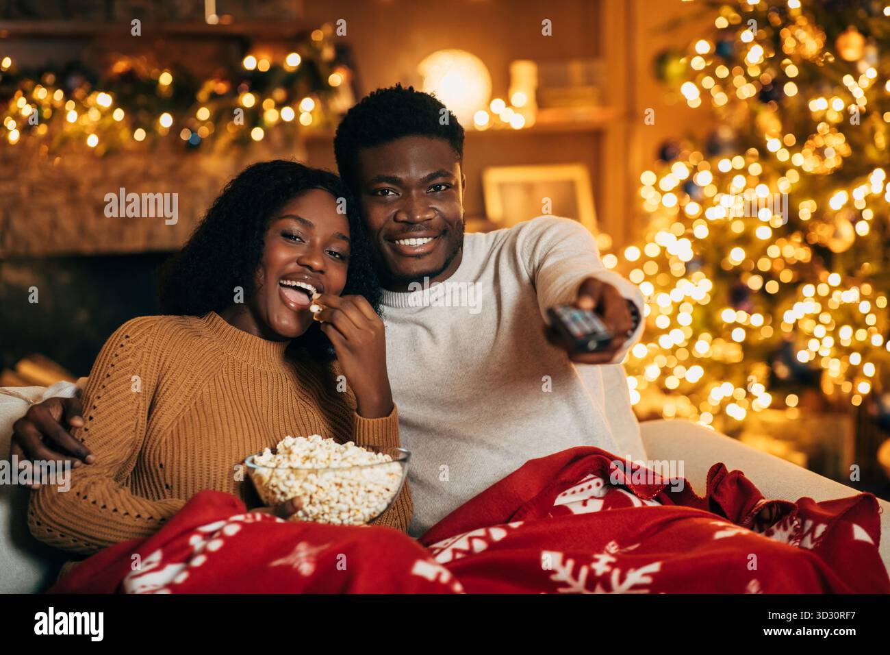 La giovane coppia si diverte con la serata del film di Natale con popcorn nell'accogliente soggiorno Foto Stock
