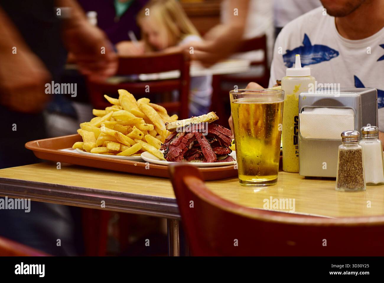 Primo piano di classici panini di pastrami impilati in alto sul pane di segale, serviti su piatti bianchi con lance di sottaceti di aneto in un ambiente gastronomico tradizionale. Perfe Foto Stock