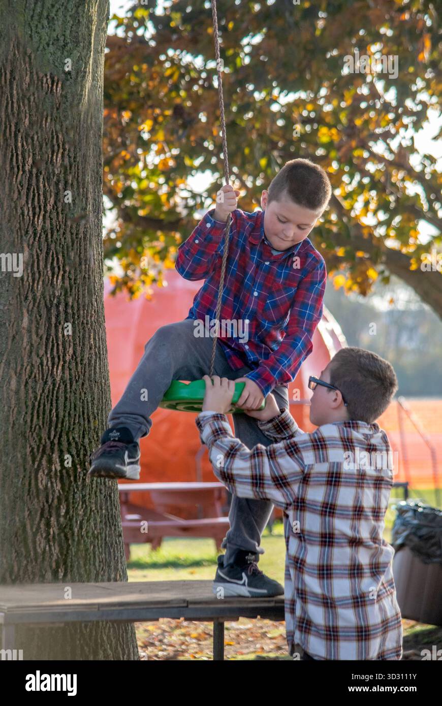 Il fratello maggiore aiuta un fratello più giovane ad entrare in sicurezza in un'oscillazione di corda Foto Stock