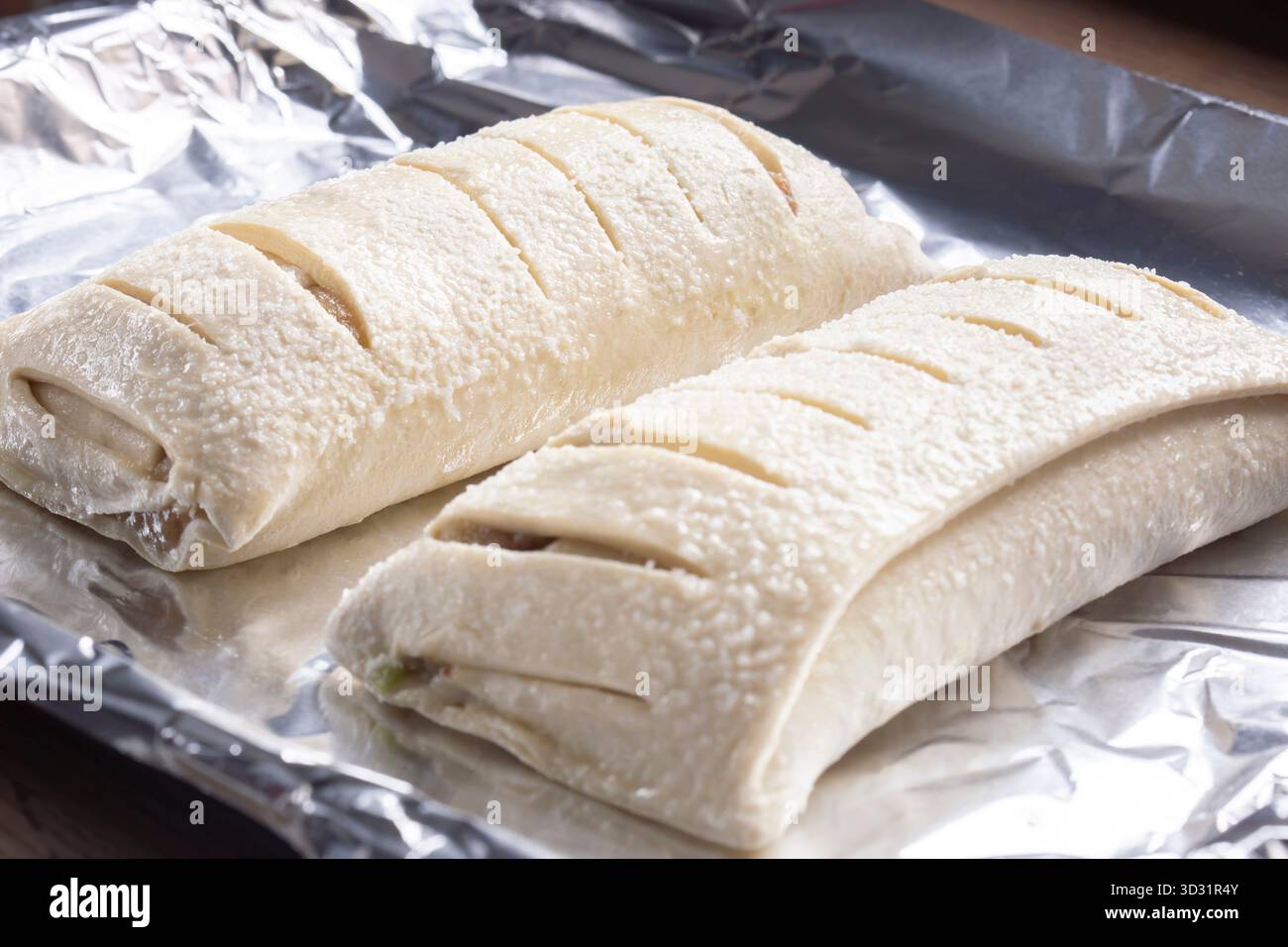 Strudels di mele crude, con pasta a fette, su foglio di alluminio pronto per la cottura in forno. Concetto di cottura in casa Foto Stock