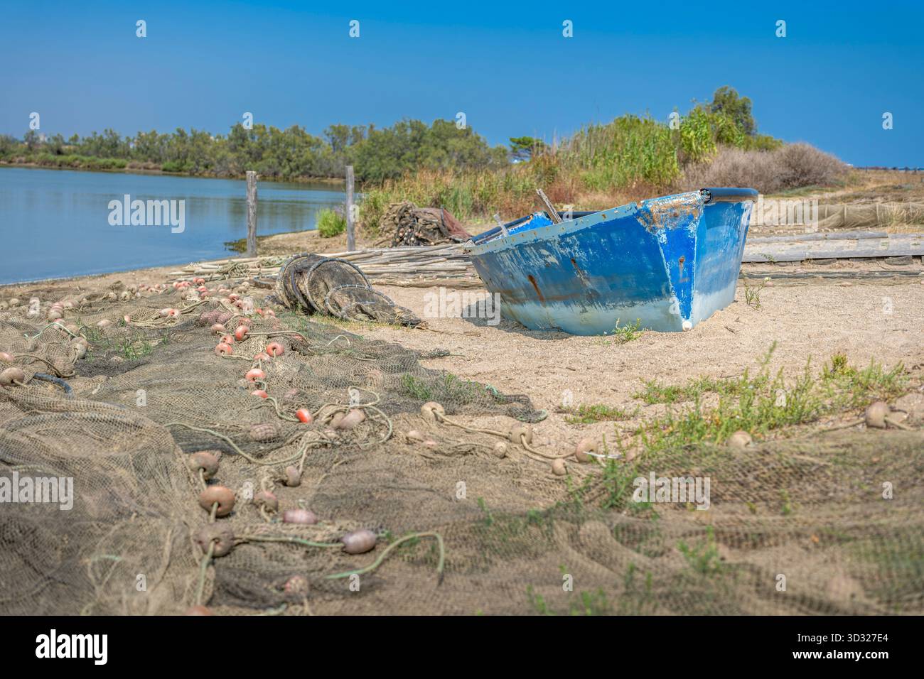 Una barca da pesca blu abbandonata e intemprata, trasportata su una spiaggia sabbiosa accanto alle reti da pesca e filata sotto un cielo blu brillante Foto Stock
