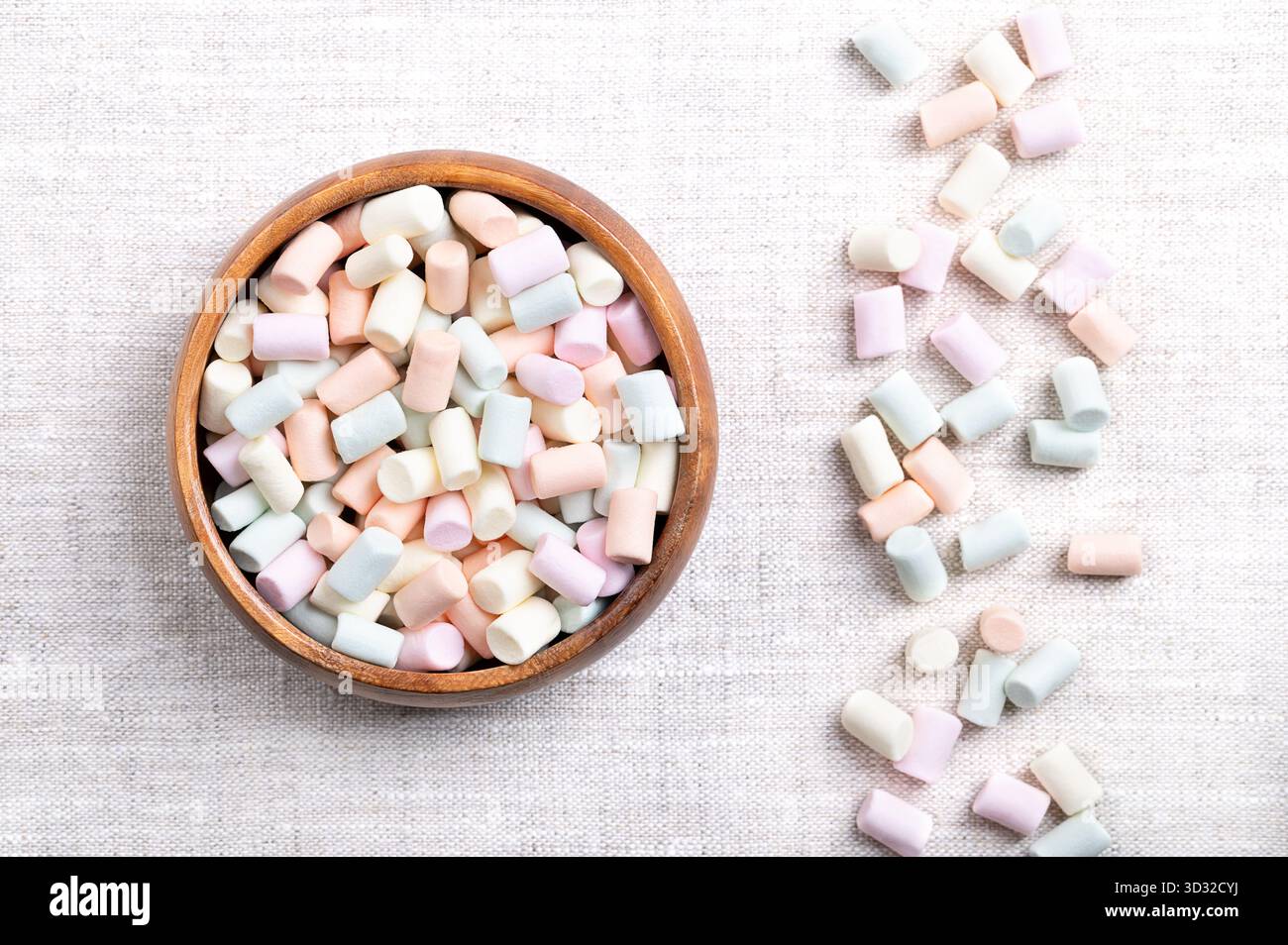 Mini marshmallow multicolori, in una ciotola di legno, su lino. Piccole porzioni di dolciumi color pastello a base di zucchero, acqua e gelatina. Foto Stock