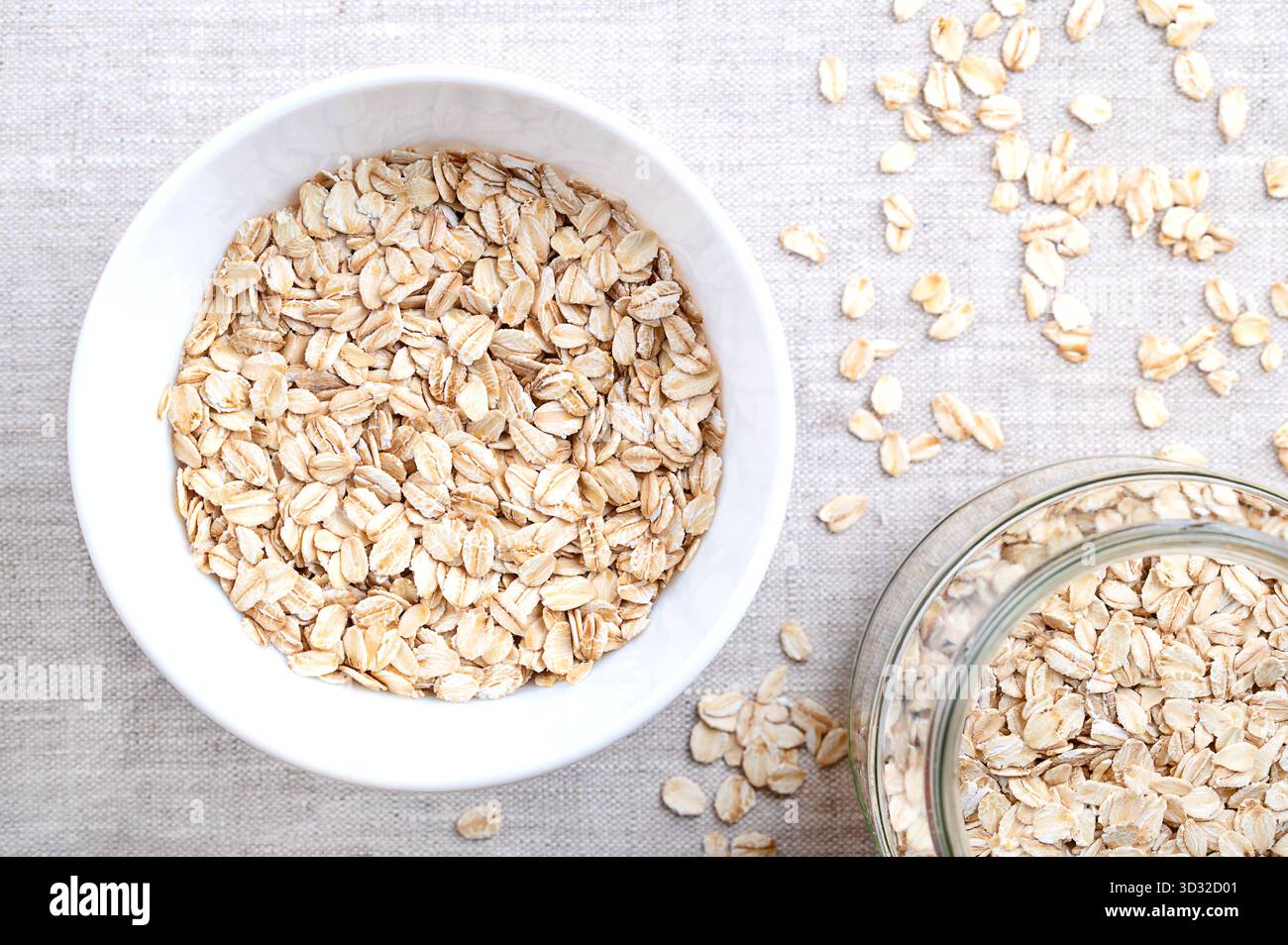 Avena arrotolata, avena spessa e vecchia, in una ciotola bianca, su lino. Semi d'avena essiccati e cotti al vapore, arrotolati in fiocchi sotto rulli pesanti. Foto Stock