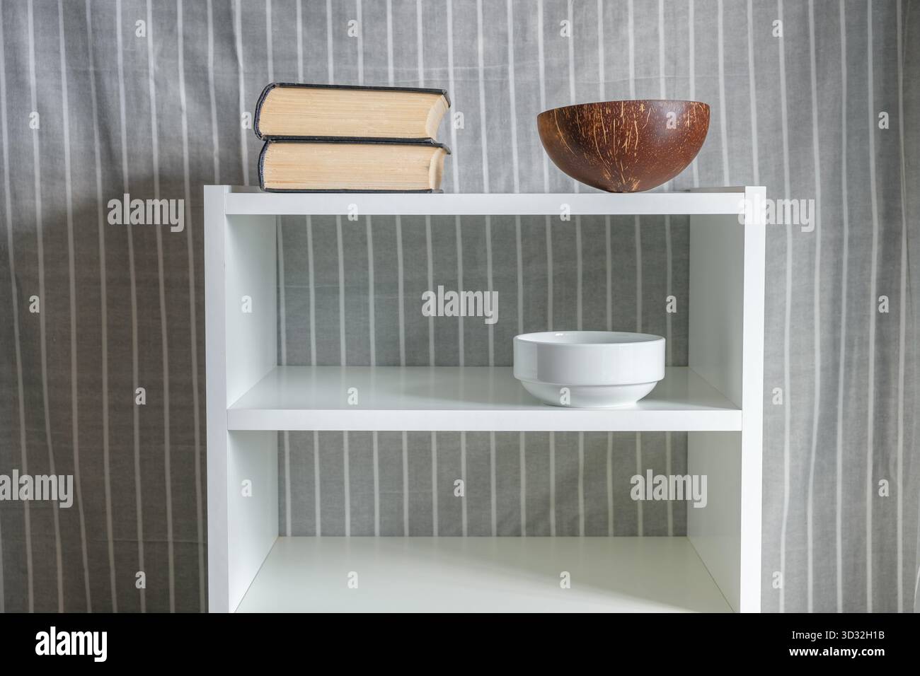 libri, vaso di cocco e ciotola su libreria bianca Foto Stock