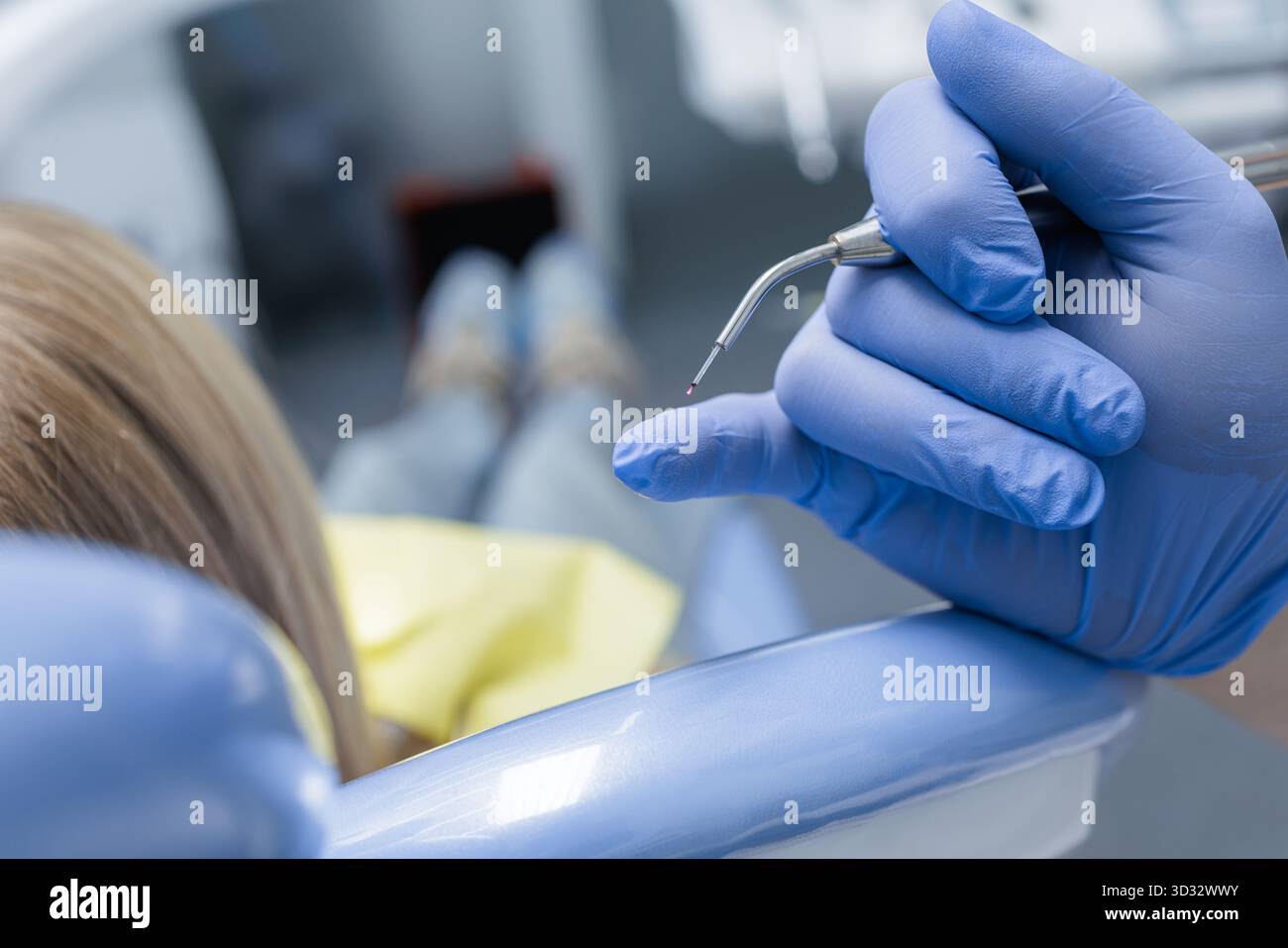 Primo piano di una punta laser a diodi in una mano con i guanti accanto a un paziente bambino, mostrando odontoiatria laser pediatrica e cure sterili. Foto Stock