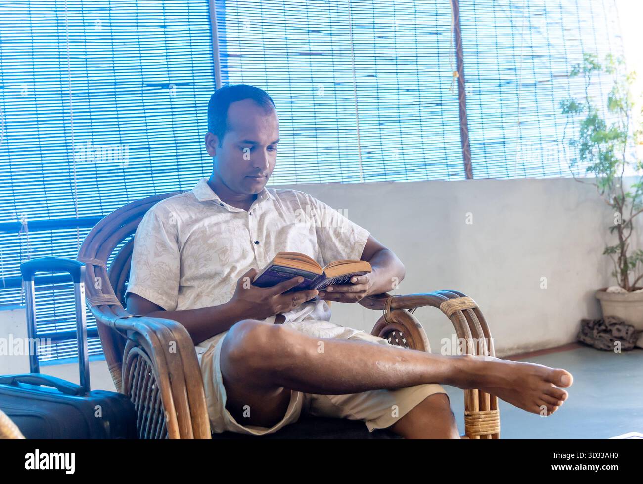 uomo in camicia bianca che si rilassa su una sedia di legno leggendo un libro al chiuso Foto Stock
