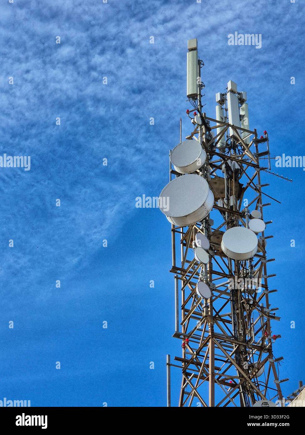 Una grande torre di comunicazione (torre di comunicazione) con numerose antenne e parabole satellitari, fotografata contro un cielo blu brillante. - Immagine stock catturata con smartphone