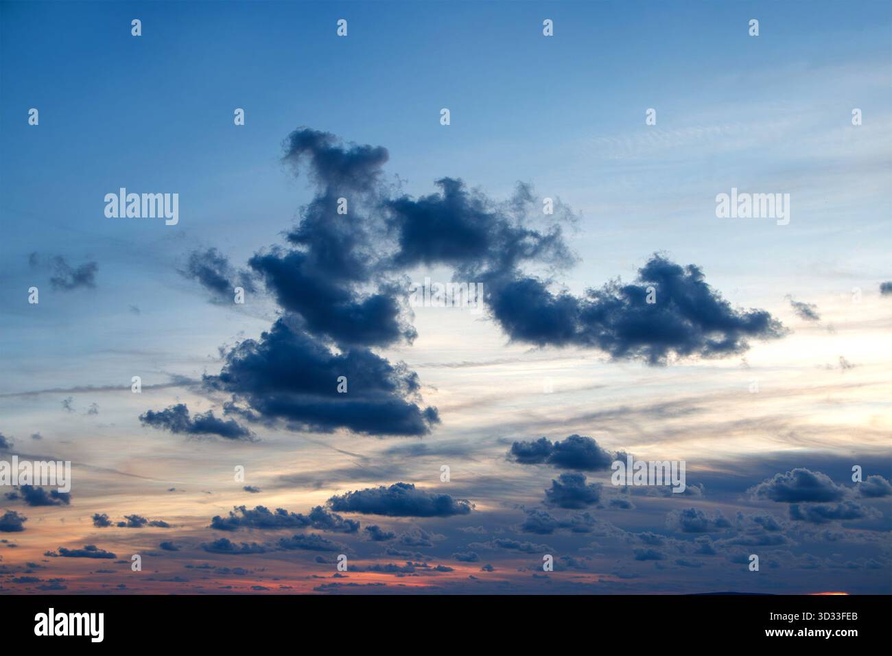 I toni blu e arancione profondi riempiono il cielo mentre le nuvole sparse si spostano sopra l'orizzonte durante un drammatico tramonto serale Foto Stock