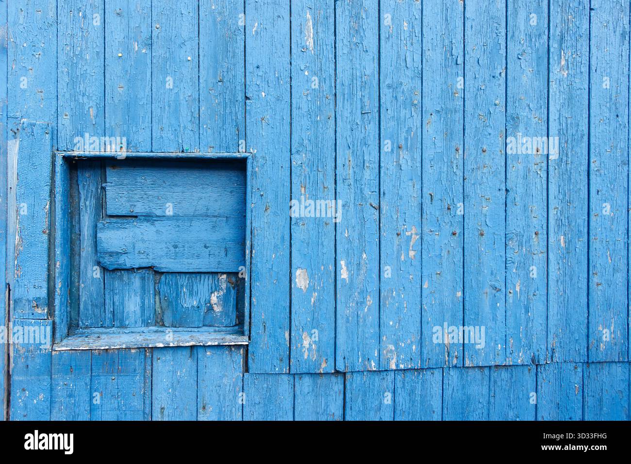 Parete di legno blu intemprata con una piccola finestra quadrata chiusa con tavole rustiche di legno disomogenee St Abbs scottish Borders scozia Foto Stock