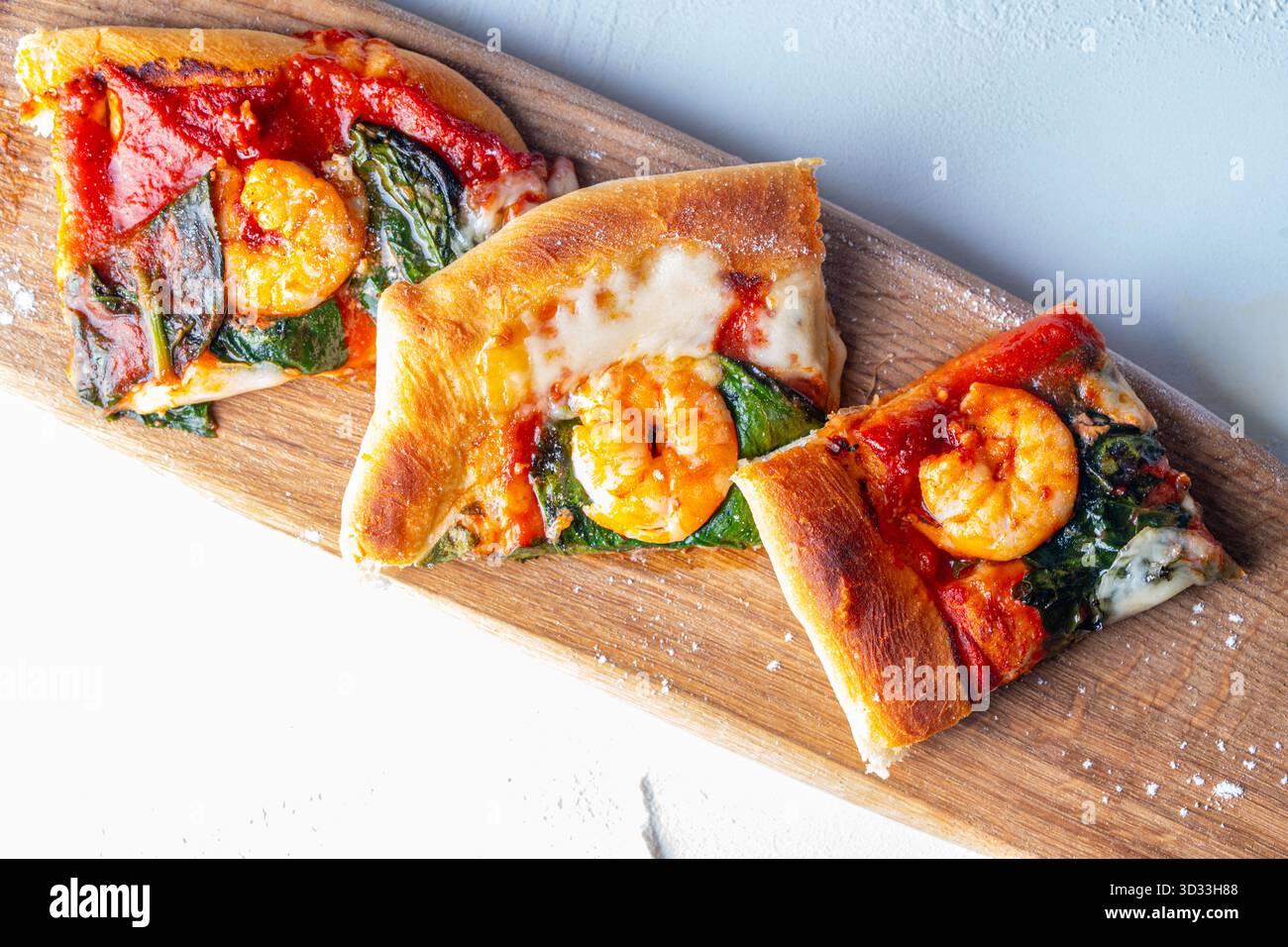 Pizza mediterranea preparata al momento con gamberetti su una tavola di legno e un tavolo bianco. Foto di alta qualità Foto Stock