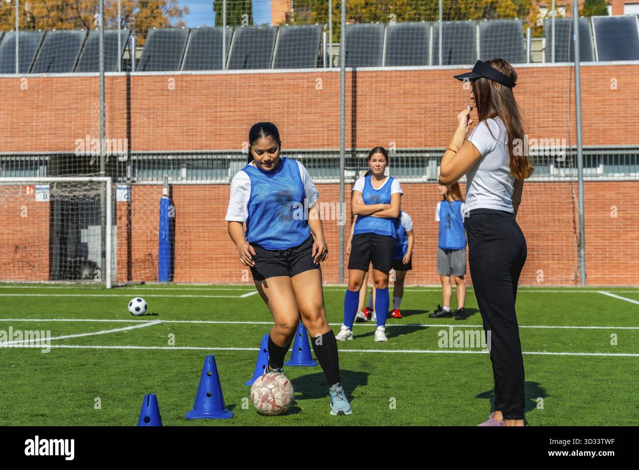 Giocatrici di calcio che ricevono istruzioni dal loro allenatore durante una sessione di allenamento su un campo di erba verde, concentrandosi sul controllo individuale della palla dri Foto Stock