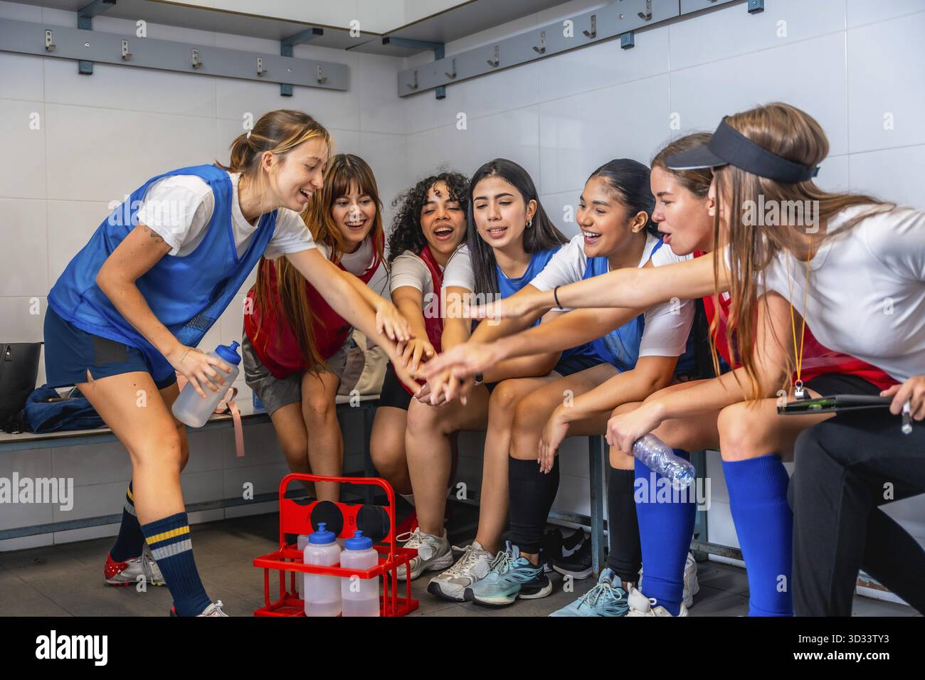 Squadra sportiva femminile che si unisce per mano in un camerino, costruendo unità, motivazione e concentrazione prima di una partita atleti energici e fiduciosi che si preparano Foto Stock