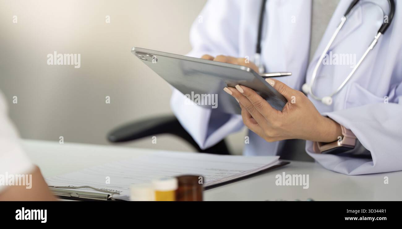 Un medico utilizza un tablet per accedere e rivedere i dati dei pazienti, migliorando l'esperienza di consultazione in una clinica moderna Foto Stock