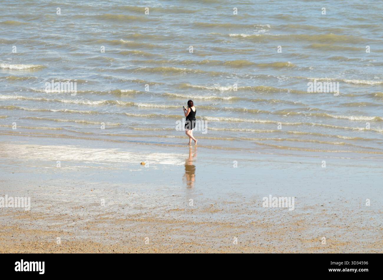 Una donna che cammina lungo la spiaggia e parla sul suo cellulare nel Regno Unito Foto Stock