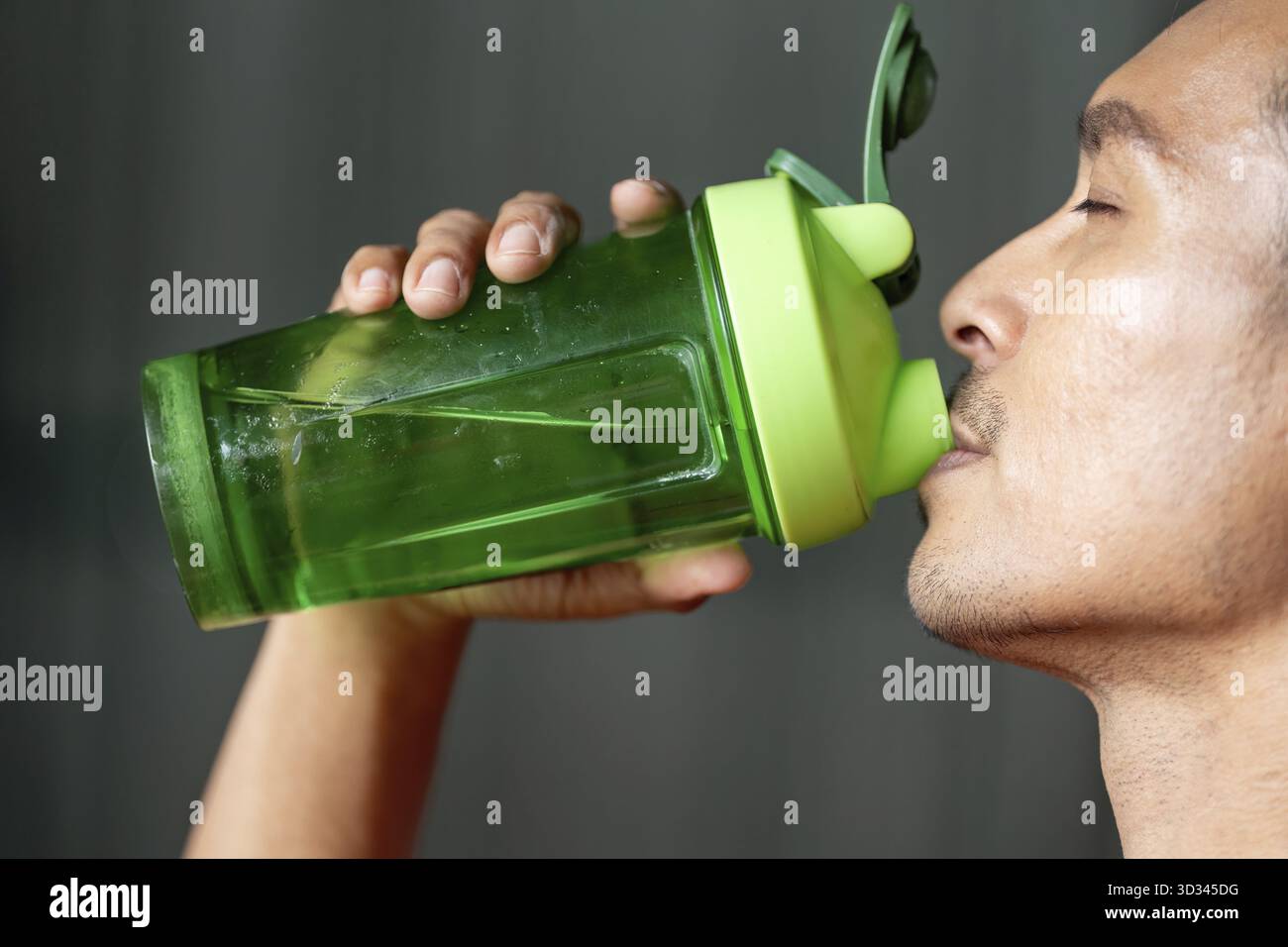 Un uomo prende un sorso rinfrescante da un biberon di shaker verde, sottolineando l'importanza dell'idratazione durante gli allenamenti Foto Stock