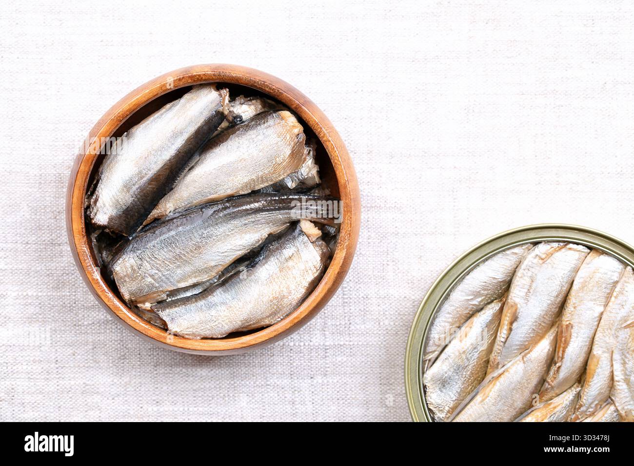 Sardine, con pelle e ossa, in olio vegetale, in una ciotola di legno, su lino. Sardine catturate allo stato brado, sardine o pilchardus in scatola. Foto Stock