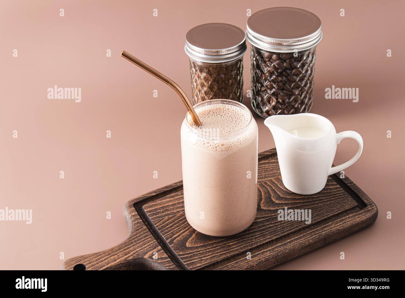 Frullato o caffè appena fatto con latte in un moderno bicchiere a forma di barattolo di birra su un tagliere di legno. Vista frontale Foto Stock