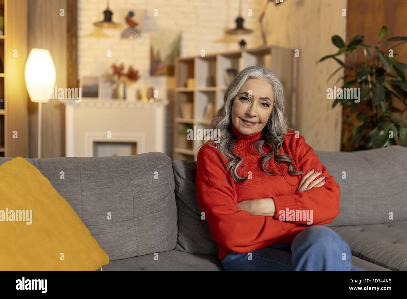 A casa. Bella donna anziana dai capelli lunghi seduta sul divano a casa Foto Stock