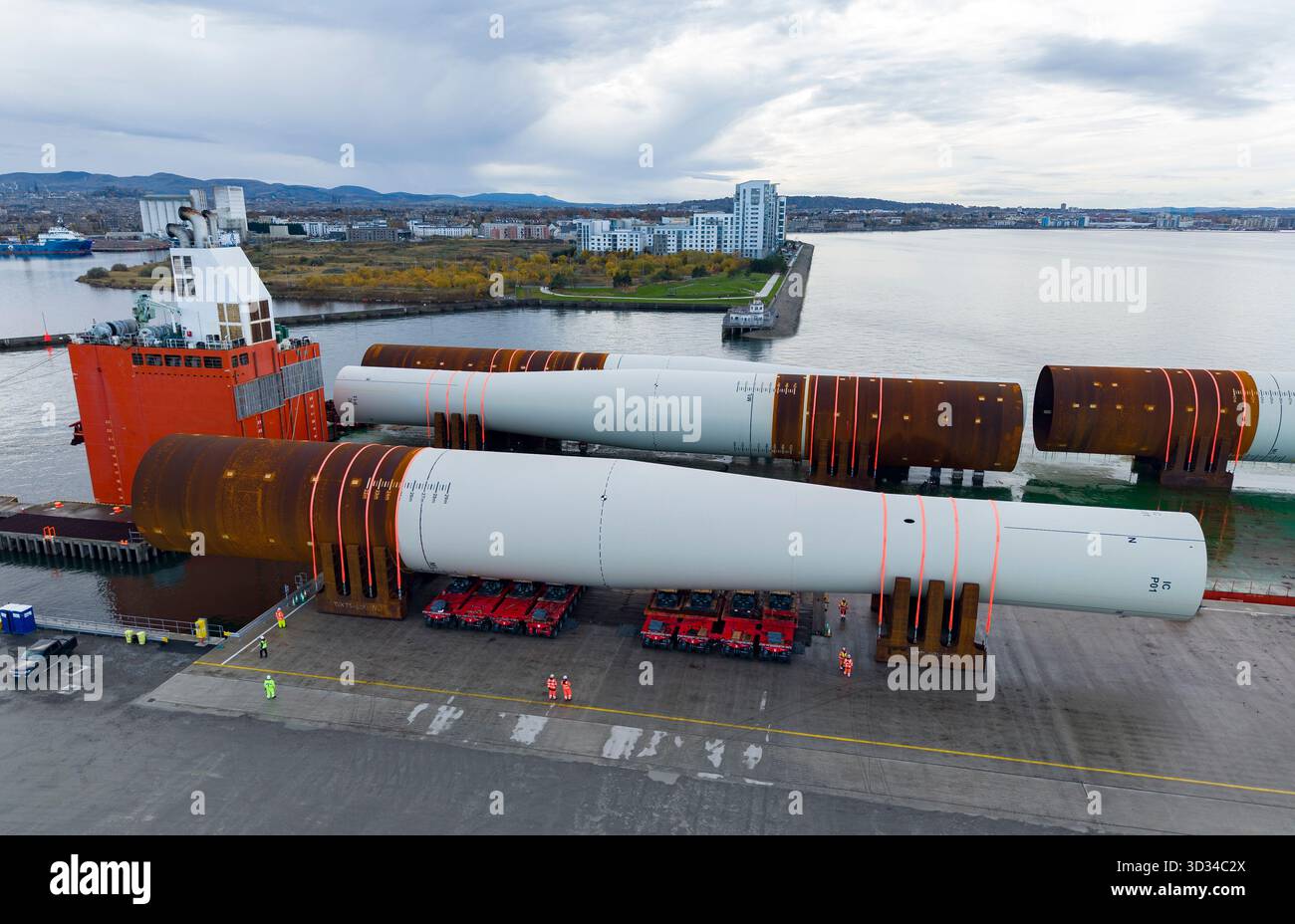 Una massiccia monopila di turbine eoliche viene scaricata e spostata da carrelli controllati da computer al porto di Leith. Le unità cinesi lunghe 110 m sono destinate Foto Stock