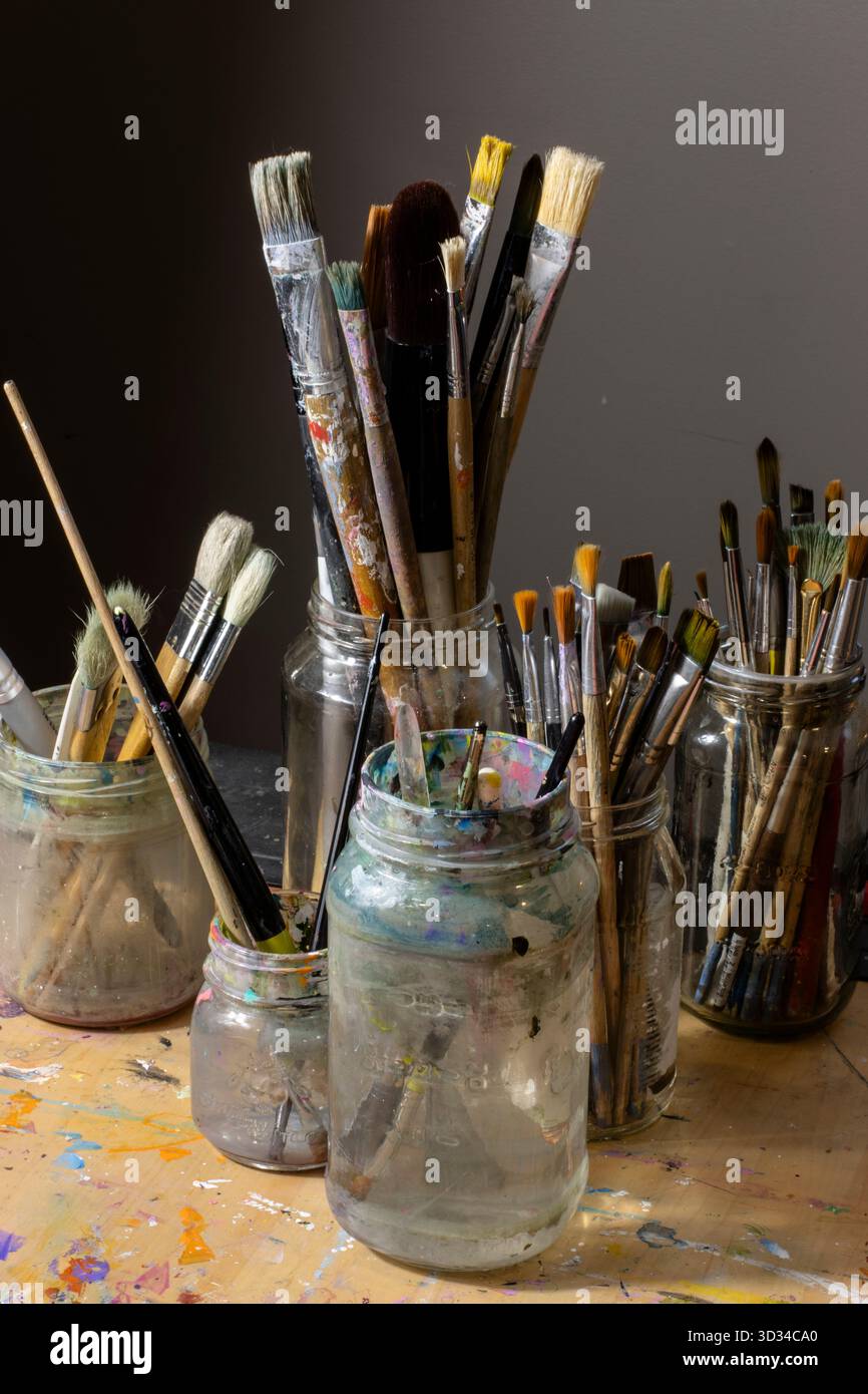 Assortimento di pennelli in vasetti di vetro sul tavolo da lavoro di un artista Foto Stock