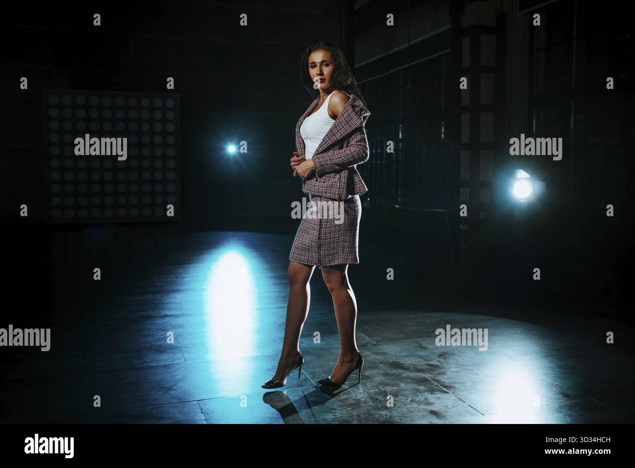 Giovane donna in stile business in piedi in interni notturni scuri con luci blu Foto Stock