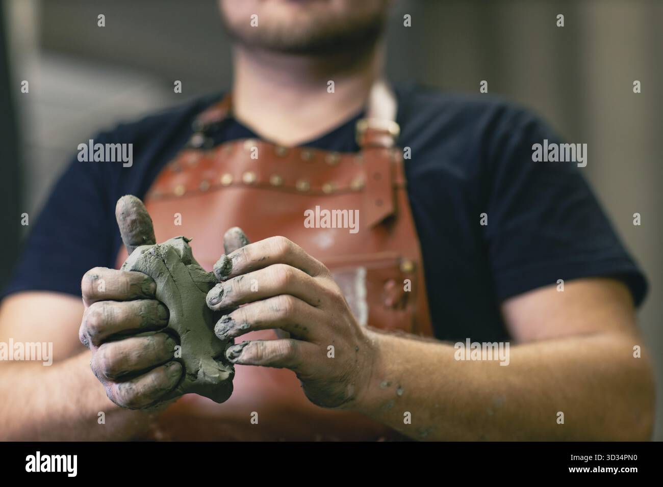 Uomo scultore vestito grembiule in pelle con argilla in mano. Laboratorio di creazione di statue artigianali Foto Stock
