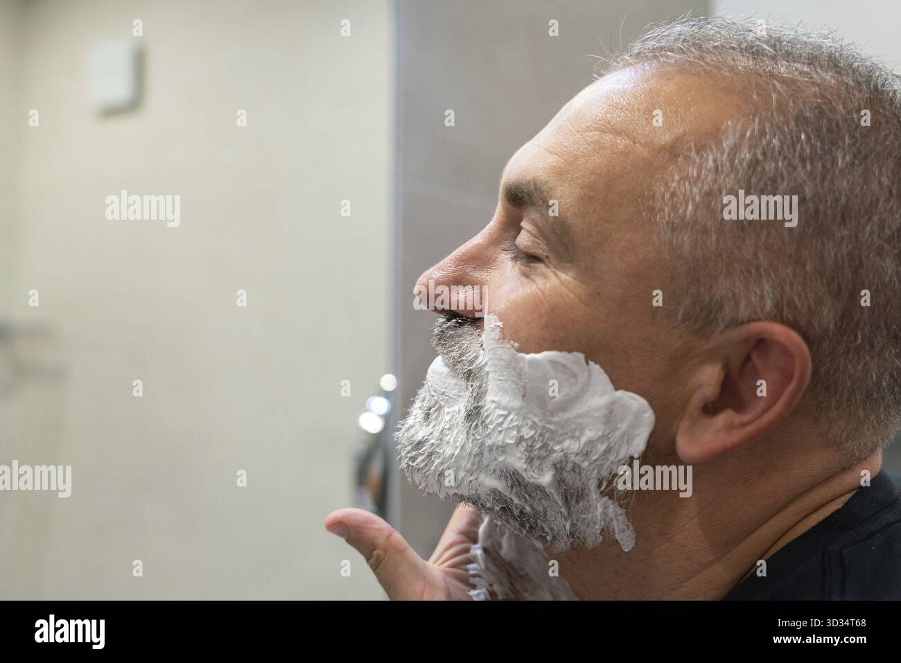 Uomo maturo e bello che applica schiuma da barba sul viso per radersi barba e baffi Foto Stock