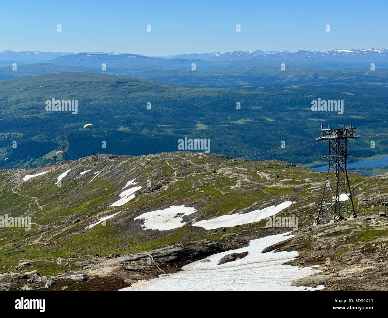 Paesaggio montano estivo a Åre, in Svezia, con i restanti innevamenti, lussureggianti pendii verdi e parapendio che si innalzano sopra la valle. - Immagine stock catturata con smartphone
