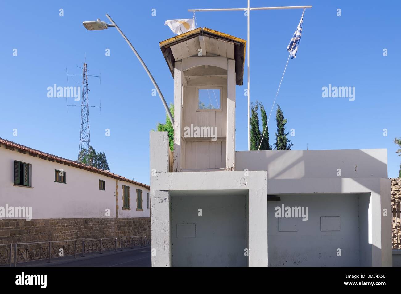 Nicosia, Cipro, piccolo palo di legno su un muro di cemento con bandiere cipriote e greche, albero radio e strada sotto un blu chiaro Foto Stock