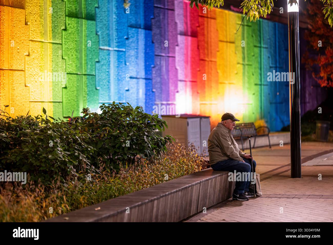 Stazione della metropolitana di Crystal City ad Arlington Virginia // ARLINGTON, VIRGINIA - il vibrante Crystal City Water Wall, un'importante installazione artistica pubblica, si trova all'ingresso della stazione della metropolitana di Crystal City. Questo iconico monumento presenta acqua che scorre su una parete testurizzata e multicolore, creando un effetto arcobaleno sorprendente. La stazione, che serve il quartiere Crystal City di Arlington, Virginia, fa parte delle linee blu e gialla della metropolitana di Washington. Crystal City è nota per la sua pianificazione urbana, i tunnel pedonali sotterranei e la vicinanza a Washington D.C. in primo piano, un uomo è se Foto Stock