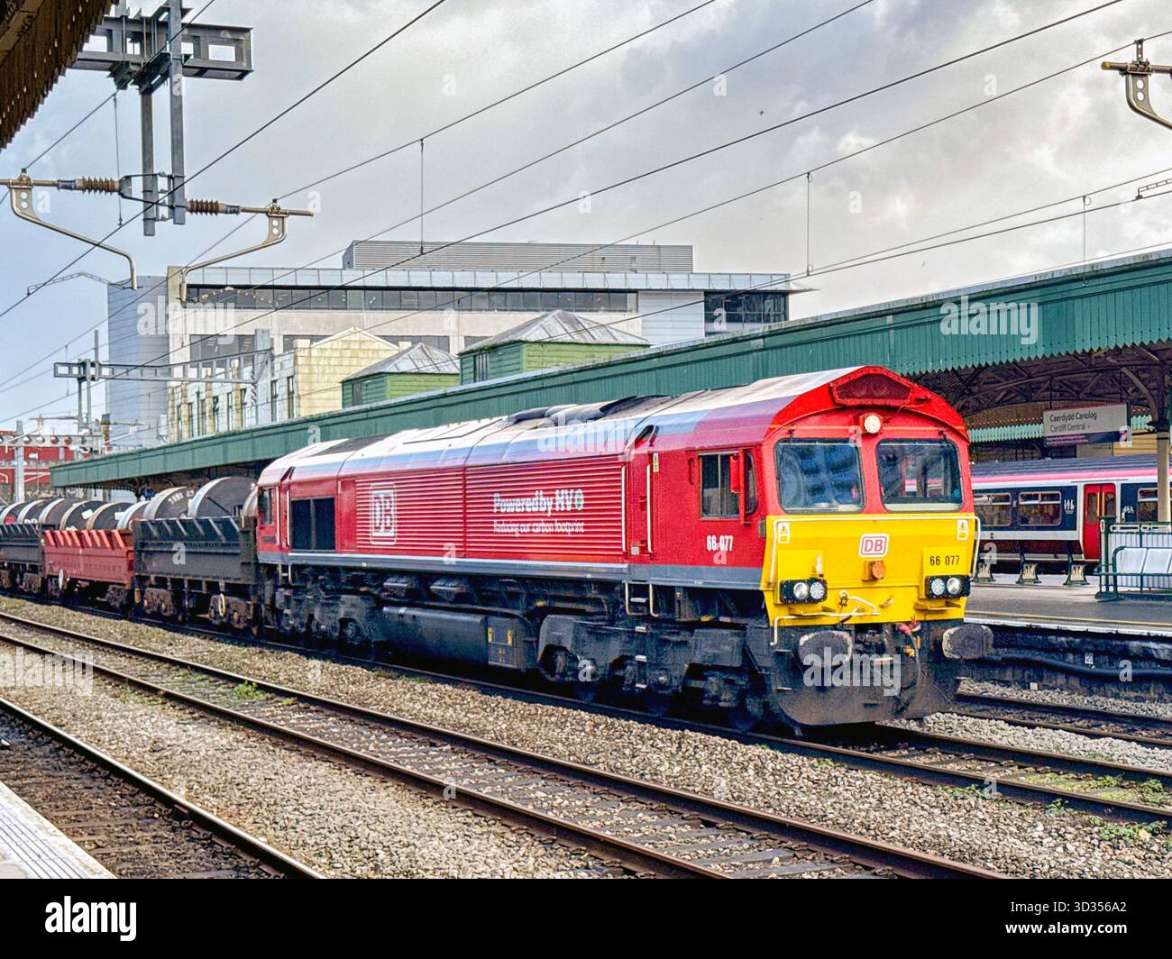 Cardiff, Galles, Regno Unito - 24 ottobre 2025: Locomotiva merci classe 66 (66 077) gestita da DB Group che trasporta un treno di carri con serpentine di acciaio pesante - Immagine stock catturata con smartphone