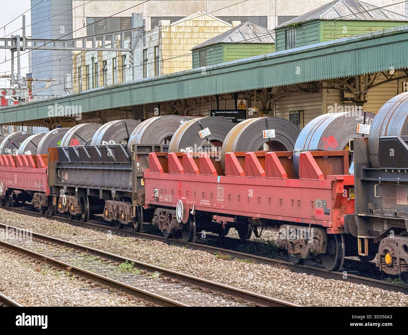 Cardiff, Galles, Regno Unito - 24 ottobre 2025: Treno di carri che trasportano serpentine di acciaio pesanti che passa attraverso la stazione centrale di Cardiff - Immagine stock catturata con smartphone