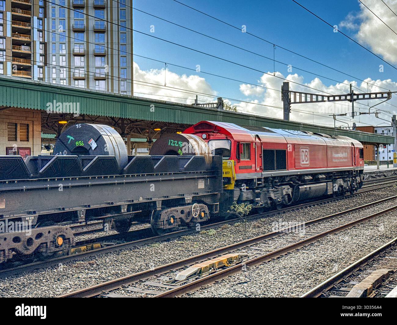 Cardiff, Galles, Regno Unito - 24 ottobre 2025: Locomotiva merci classe 66 (66 077) gestita da DB Group che trasporta un treno di carri con serpentine di acciaio pesante - Immagine stock catturata con smartphone