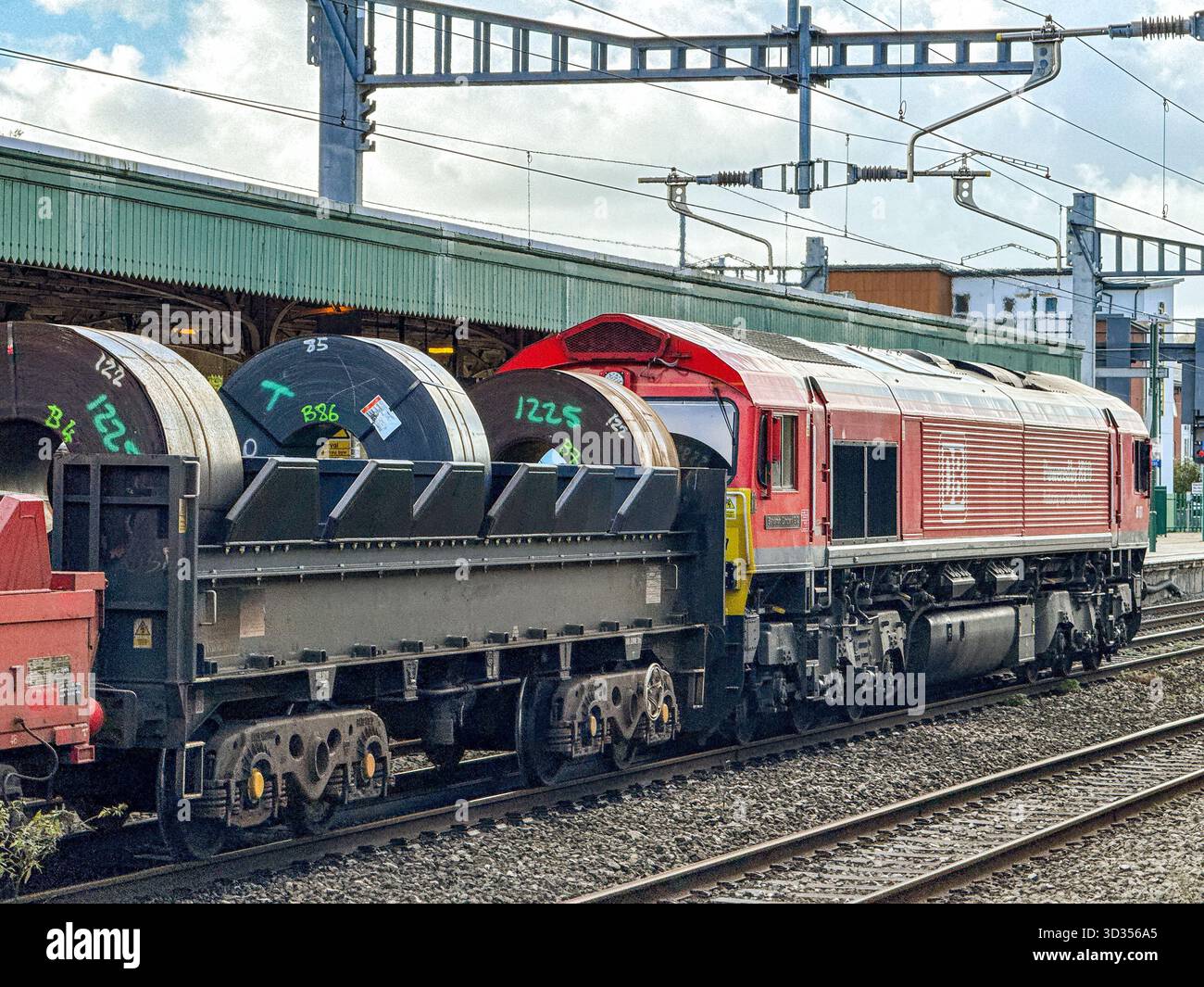 Cardiff, Galles, Regno Unito - 24 ottobre 2025: Locomotiva merci classe 66 (66 077) gestita da DB Group che trasporta un treno di carri con serpentine di acciaio pesante - Immagine stock catturata con smartphone