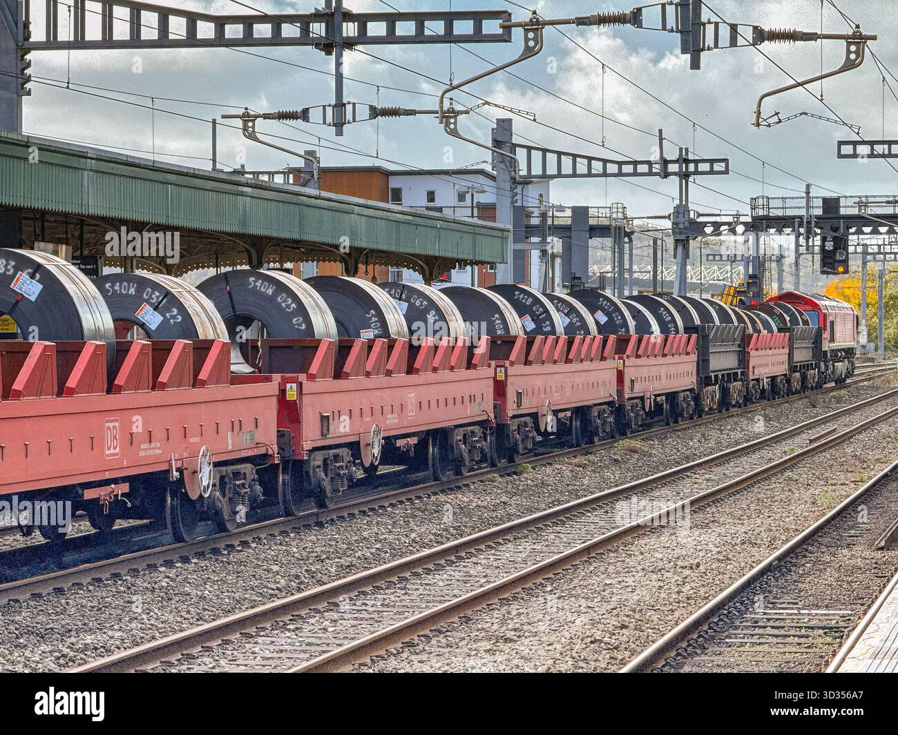 Cardiff, Galles, Regno Unito - 24 ottobre 2025: Locomotiva merci classe 66 (66 077) gestita da DB Group che trasporta un treno di carri con serpentine di acciaio pesante - Immagine stock catturata con smartphone