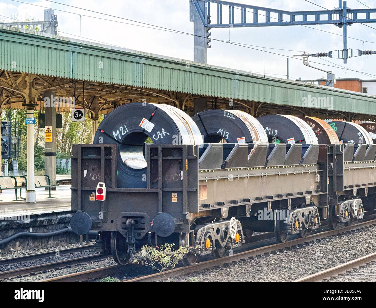 Cardiff, Galles, Regno Unito - 24 ottobre 2025: Treno di carri che trasportano serpentine di acciaio pesanti che passa attraverso la stazione centrale di Cardiff - Immagine stock catturata con smartphone