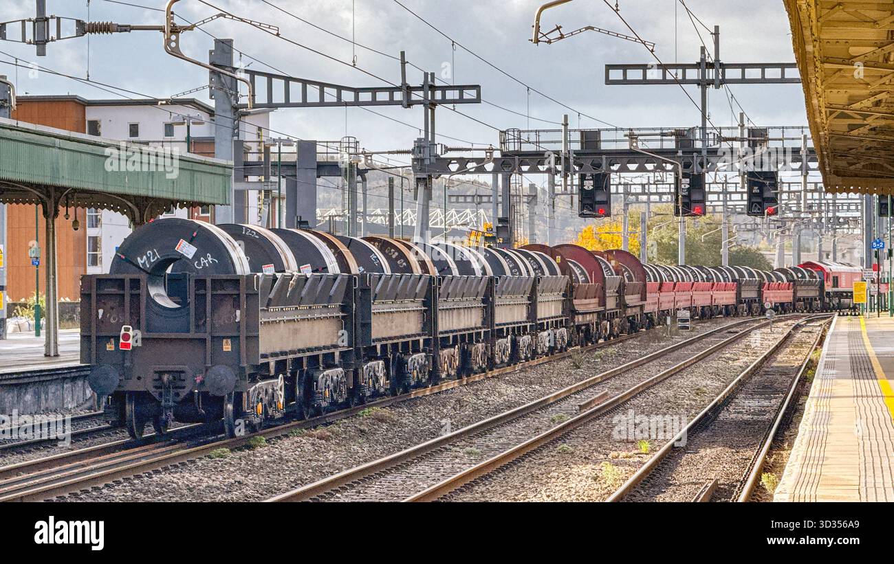 Cardiff, Galles, Regno Unito - 24 ottobre 2025: Locomotiva merci classe 66 (66 077) gestita da DB Group che trasporta un treno di carri con serpentine di acciaio pesante - Immagine stock catturata con smartphone