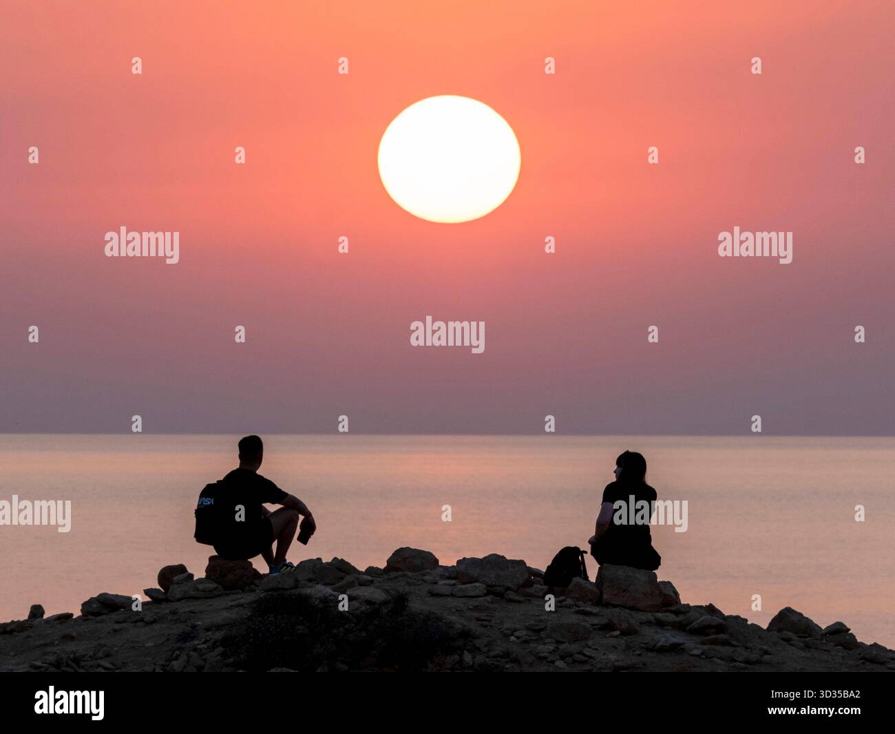 Una coppia guarda il sole tramontare da un punto panoramico sulla costa di Paphos, Cipro. Foto Stock