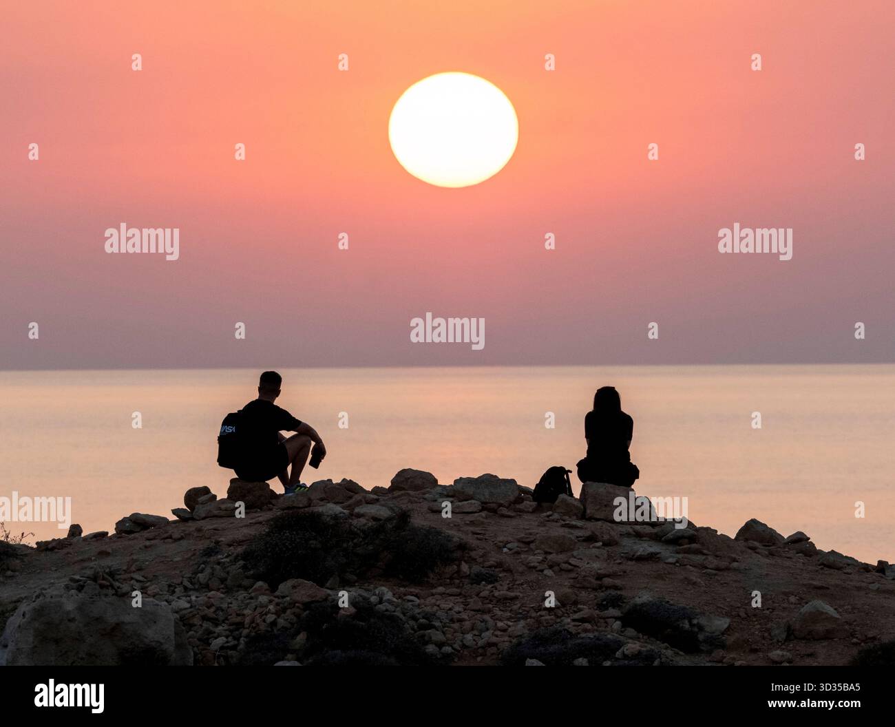 Una coppia guarda il sole tramontare da un punto panoramico sulla costa di Paphos, Cipro. Foto Stock