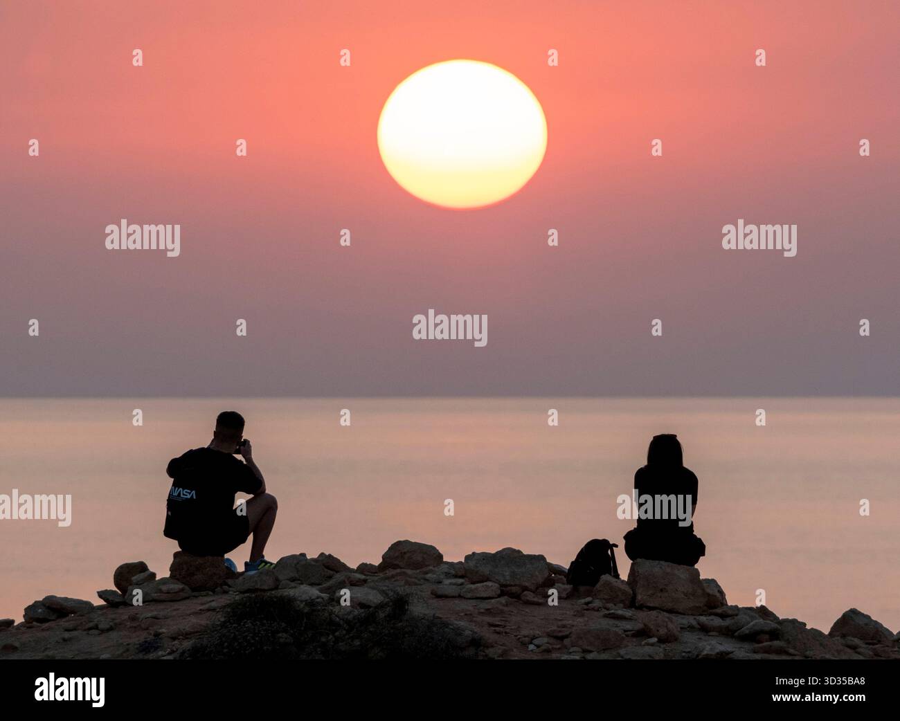 Una coppia guarda il sole tramontare da un punto panoramico sulla costa di Paphos, Cipro. Foto Stock