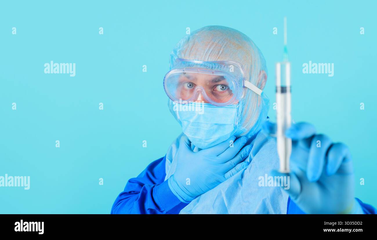 Medico in maschera medica e occhiali protettivi con siringa, fuoco selettivo. Infermiere maschio in uniforme, guanti in gomma, cappuccio chirurgico con preparazione siringa Foto Stock