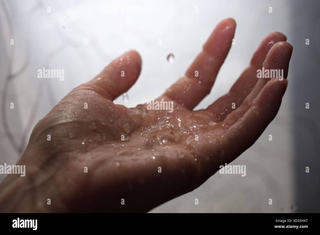 Primo piano di una palma umana tenuta in mano sotto gocce d'acqua cadenti. Un momento tattile e intimo che cattura texture, umidità e chiarezza. Foto Stock