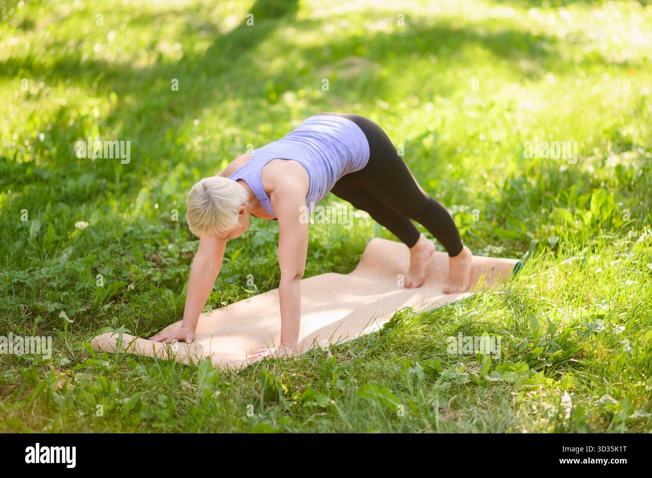 La donna di mezza età esercita e fa esercizi di rafforzamento del nucleo. La donna anziana pratica fitness e yoga all'aperto nel parco nelle giornate di sole Foto Stock
